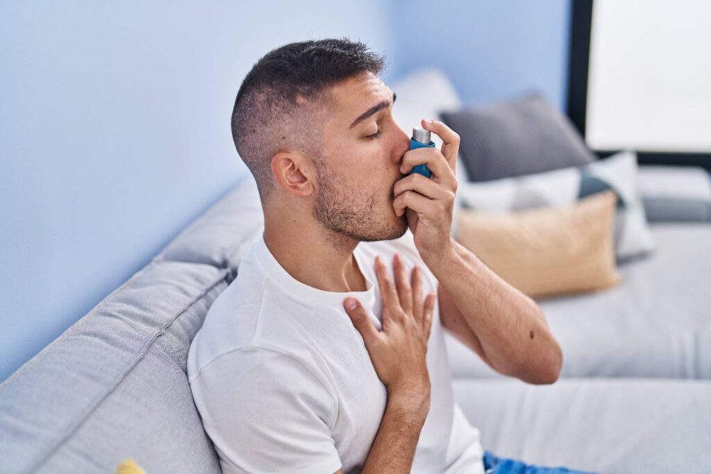 young-hispanic-man-using-inhaler-sitting-sofa-home (1)